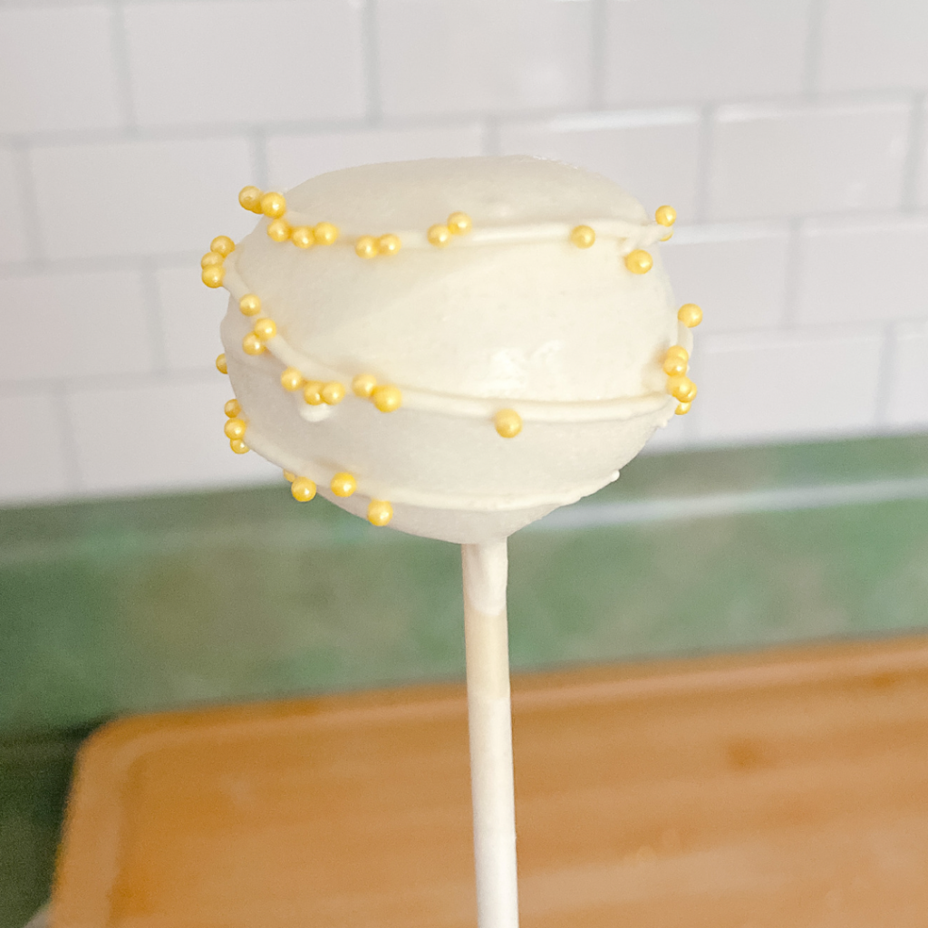 Upright lemon cake pop covered in vanilla chocolate and sprinkles